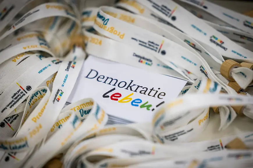 Visitenkarten mit Aufdruck "Demokratie leben!" inmitten zahlreicher Bändchen mit Aufdruck "Programmkonferenz Demokratie leben!"