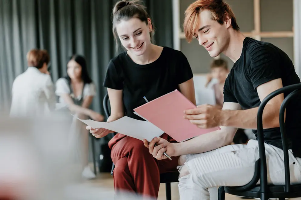 Zwei Personen auf Stühlen schauen in Dokumente