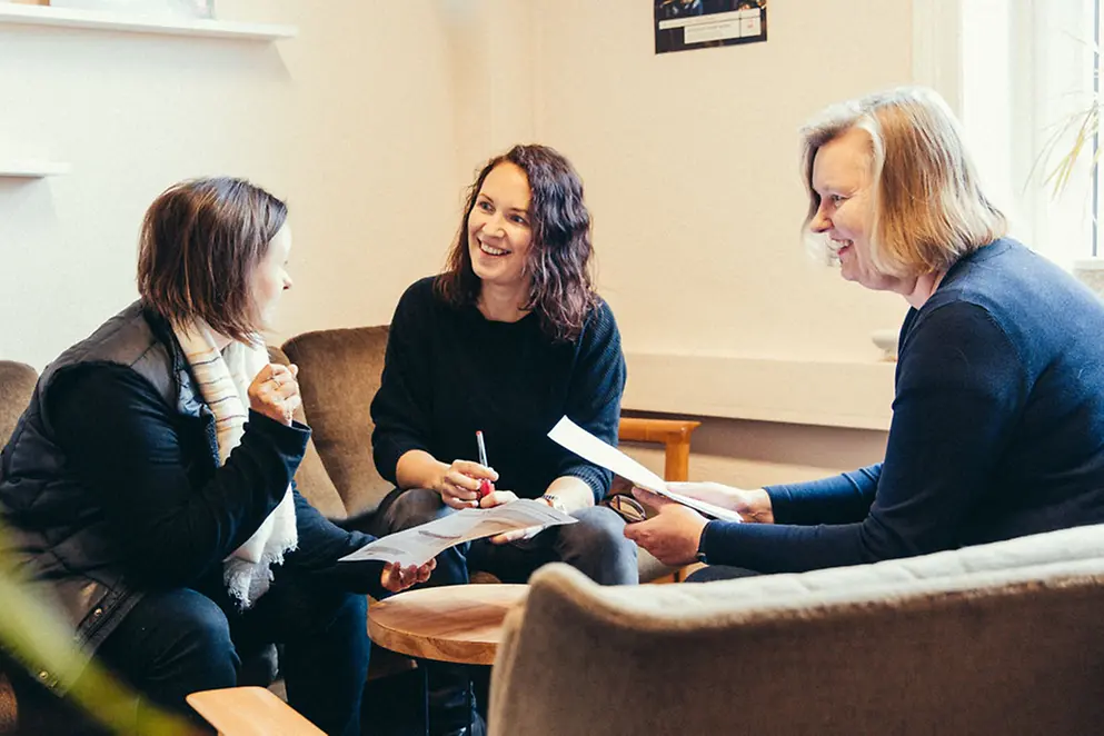 Drei Frauen sitzen um einen Tisch herum und unterhalten sich angeregt.