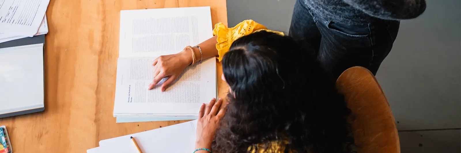 Eine Frau schaut einer anderen Frau über die Schulter, die an einem Tisch sitzt und liest.
