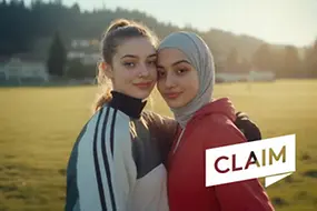 Zwei junge Frauen – eine mit Kopftuch – gucken in die Kamera