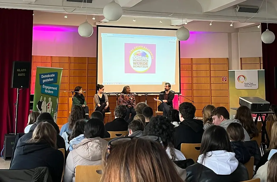 Vier Personen befinden sich auf einem Podium im Gespräch.