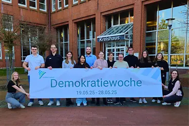 Junge Menschen stehen vor dem Kreishaus und halten ein Banner mit der Aufschrift "Demokratiewoche 2025"