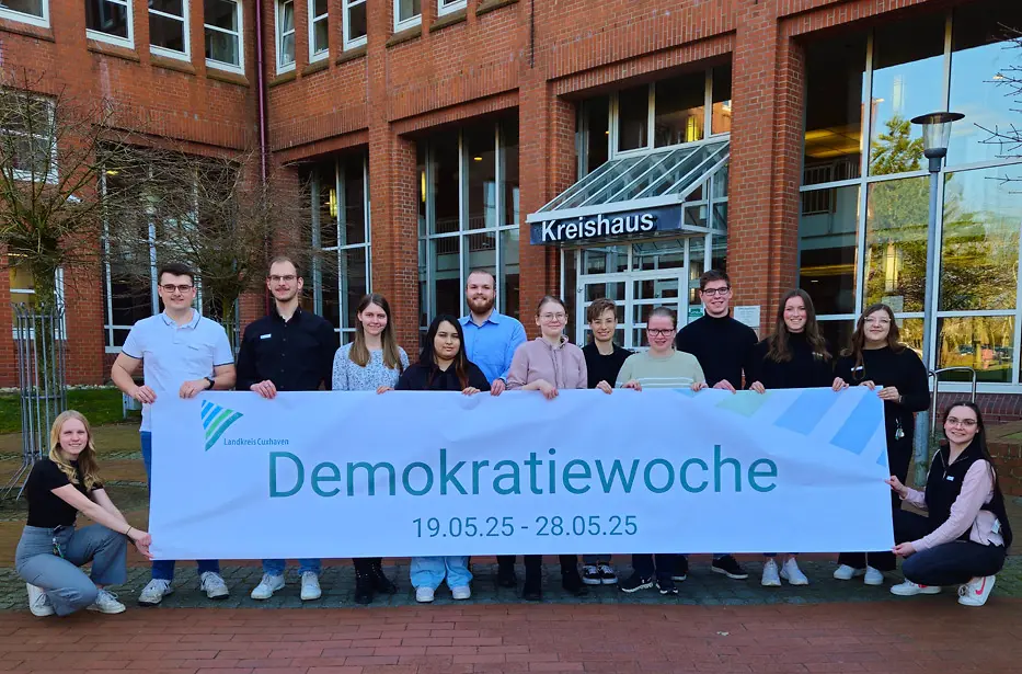 Junge Menschen stehen vor dem Kreishaus und halten ein Banner mit der Aufschrift "Demokratiewoche 2025"