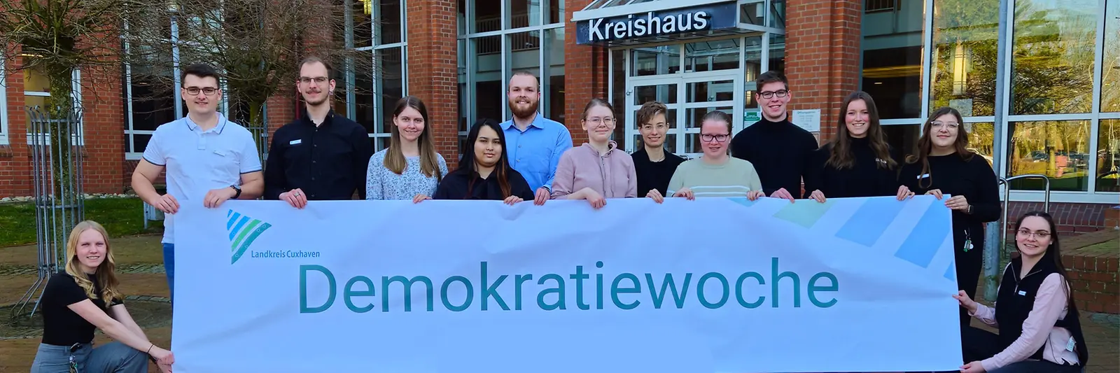 Junge Menschen stehen vor dem Kreishaus und halten ein Banner mit der Aufschrift "Demokratiewoche 2025"