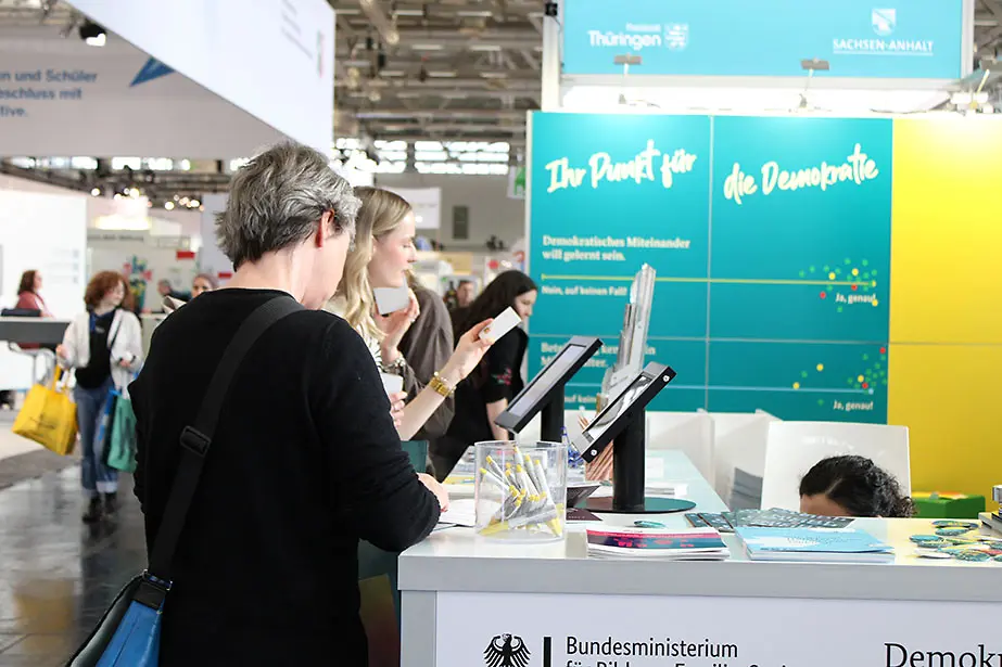 Drei Personen betrachten die Materialien am Messestand von "Demokratie leben!"