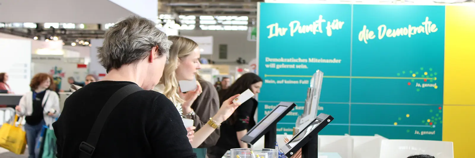 Drei Personen betrachten die Materialien am Messestand von "Demokratie leben!"